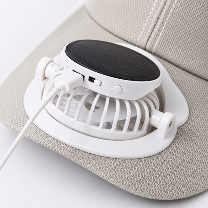 A white portable mini fan with a black solar panel top, shown mounted on the brim of a beige textured baseball cap.